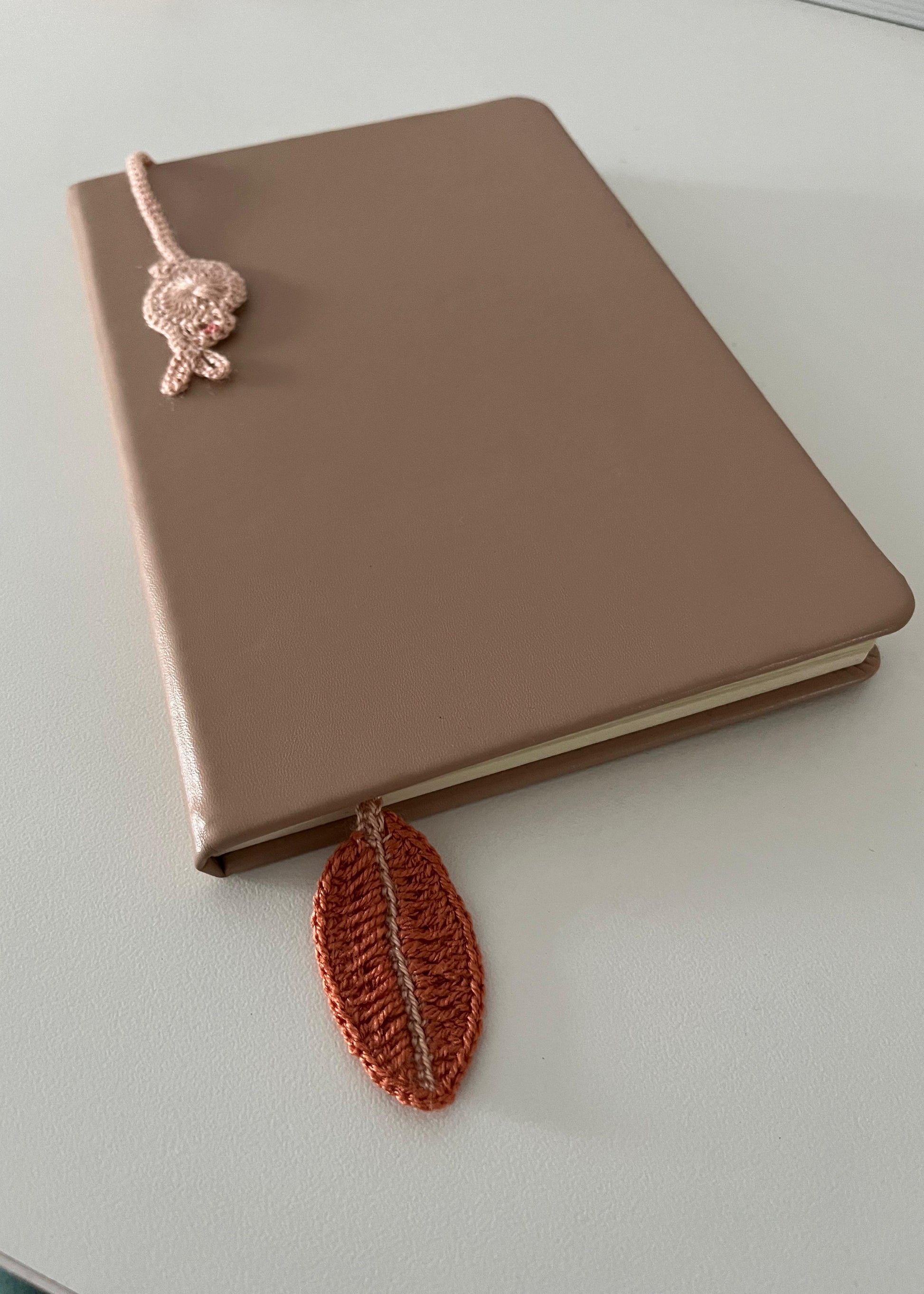 Brown notebook with a pink knitted bookmark on a light gray surface